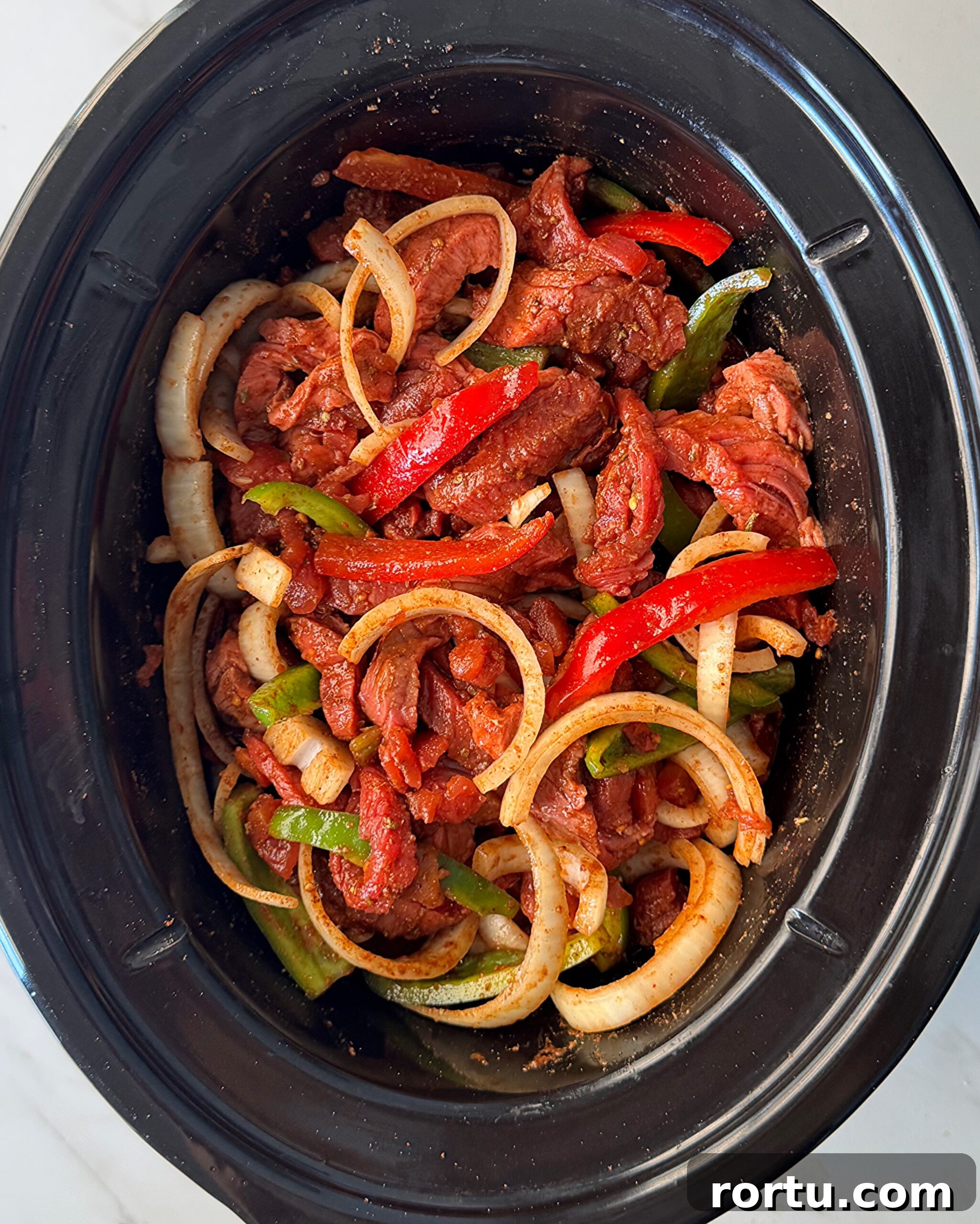 overhead shot of uncooked steak fajitas in a black slow cooker