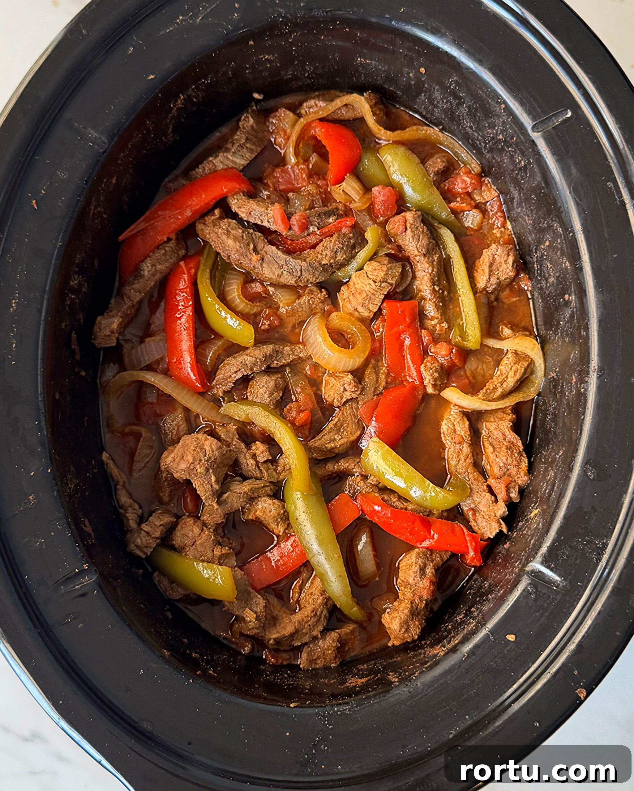 overhead shot of cooked steak fajitas in a black slow cooker