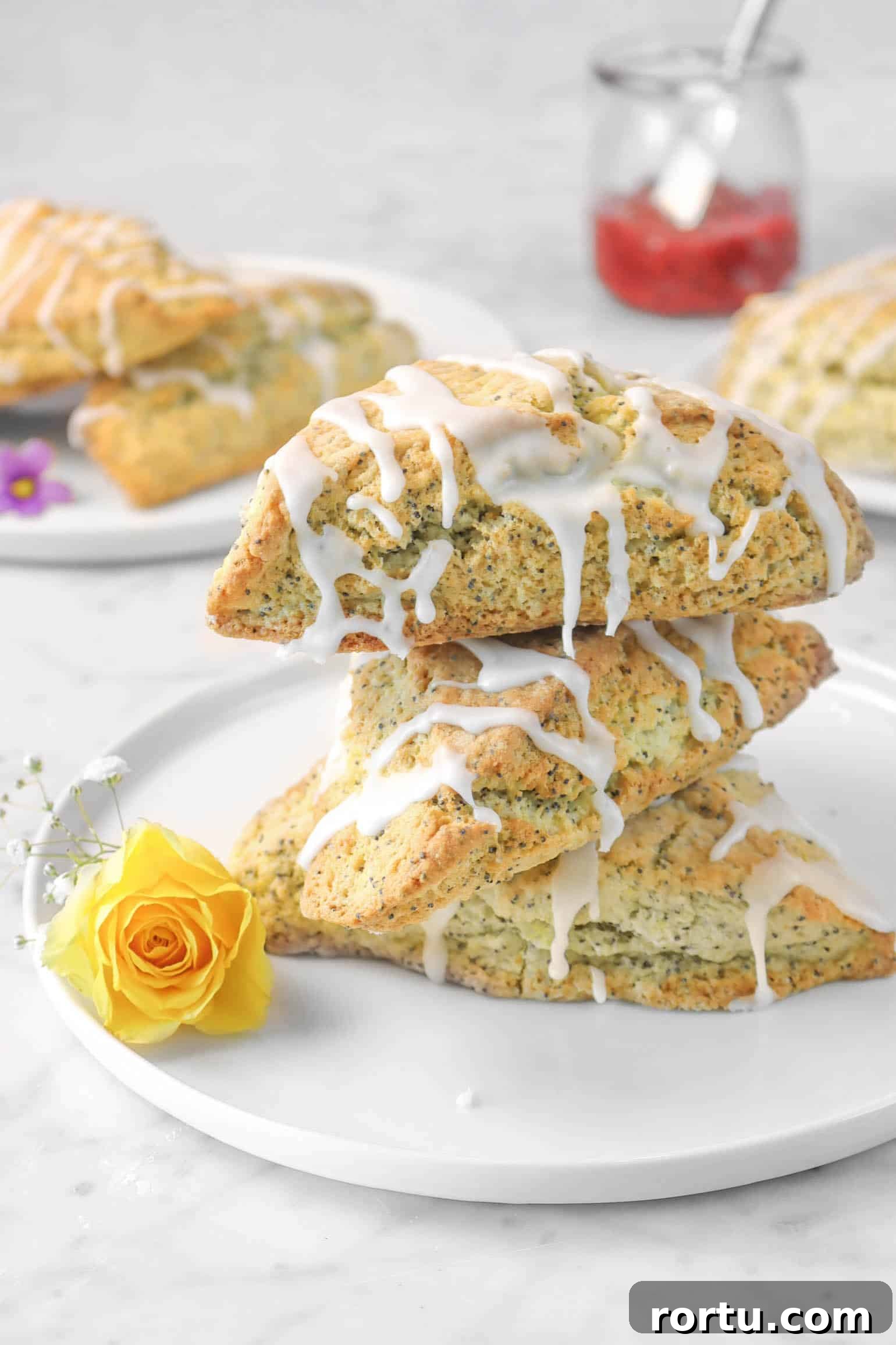 Giant Lemon Poppy Seed Scones — Soft, Zesty Breakfast Treat 13 three lemon poppyseed scones with fresh flowers, more scones in the back, and a jar of jam