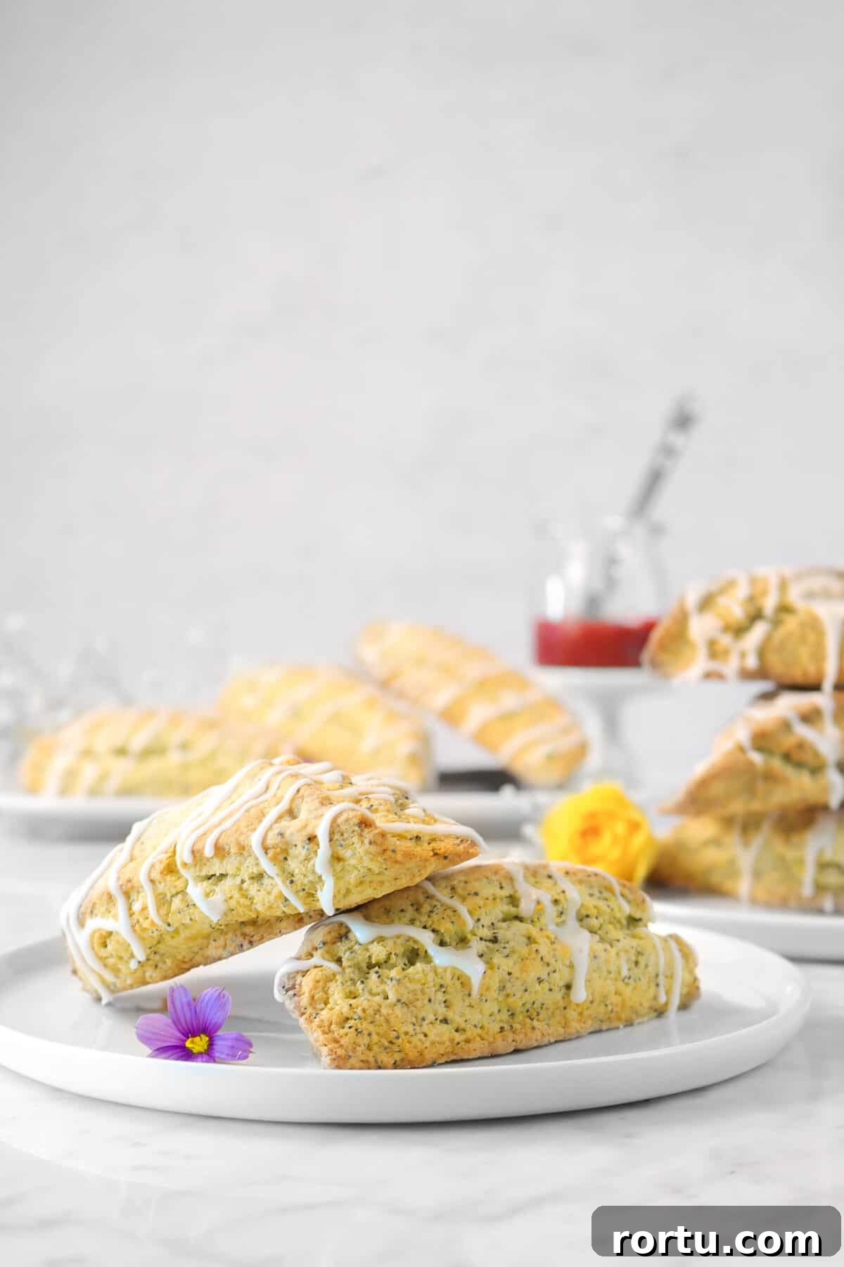 Giant Lemon Poppy Seed Scones — Soft, Zesty Breakfast Treat 3 two lemon poppyseed scones on a white plate with fresh flowers and more scones in the background