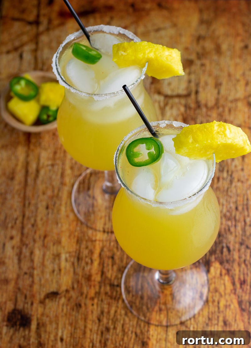 overhead of two cocktails with pineapple ice and jalapeño - recipe sweet hot mama