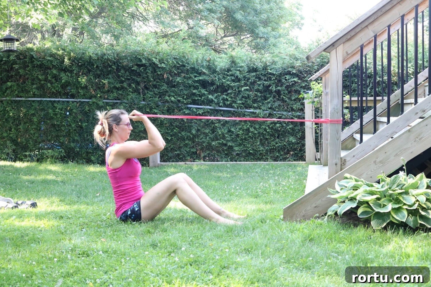 10 Targeted Exercises for Bat Wings + a 10-Minute Arm Routine 3 Woman in pink shirt and black shorts performing a bicep curl with a resistance band outside