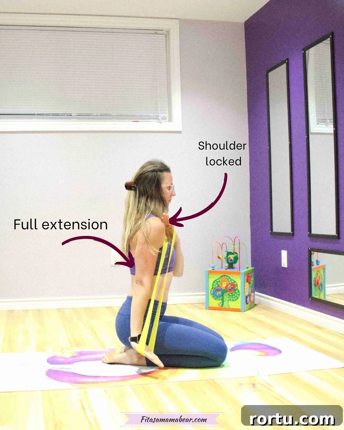 10 Targeted Exercises for Bat Wings + a 10-Minute Arm Routine 5 woman in purple sports bra and blue pants kneeling on a yoga mat holding a yellow mini loop on her shoulder and performing a tricep extension