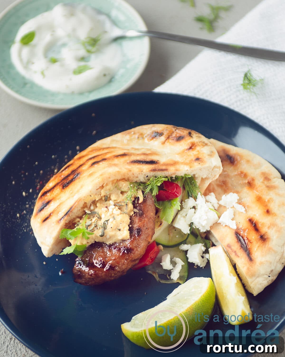 Greek-Style Burgers with Feta and Tzatziki Recipe 10 A blue plate with grilled vegetables, hamburger and feta cheese.