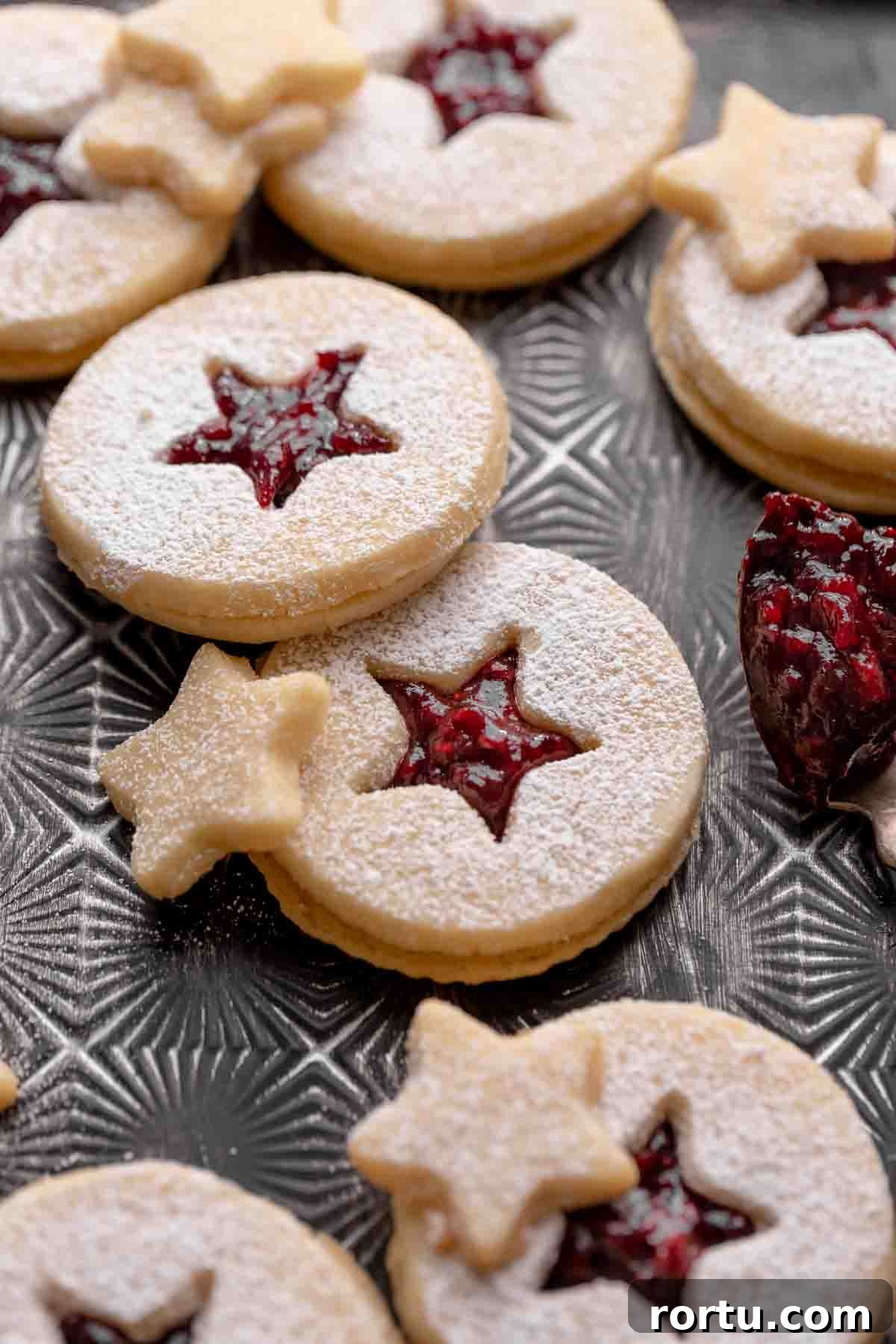 Raspberry Jam Linzer Shortbread Cookies: Classic Sandwich Recipe 2 raspberry linzer cookies filled with jam and dusted with powdered sugar on a black tray.