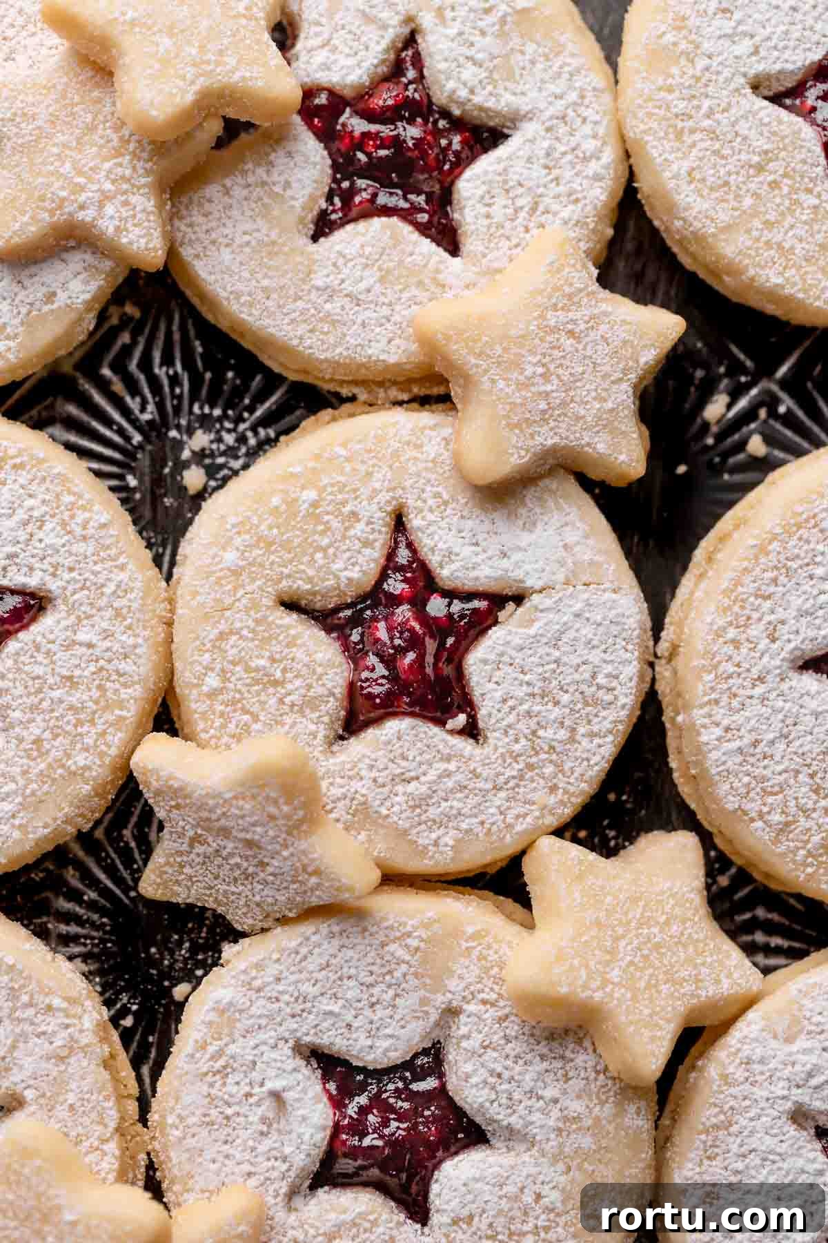 Raspberry Jam Linzer Shortbread Cookies: Classic Sandwich Recipe 3 linzer tart cookies with raspberry jam on a black baking tray.