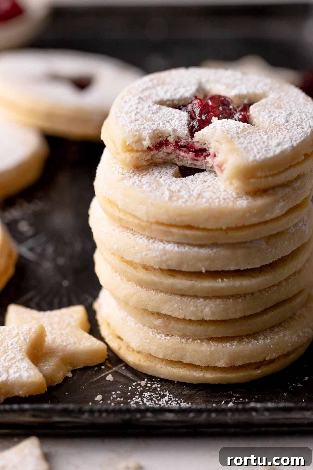 Raspberry Jam Linzer Shortbread Cookies: Classic Sandwich Recipe 8 a stack of raspberry linzer cookies on a black baking tray.