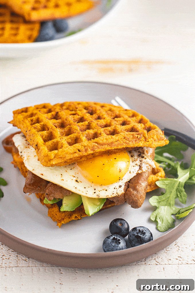A plate with a sweet potato waffle breakfast sandwich and blueberries.
