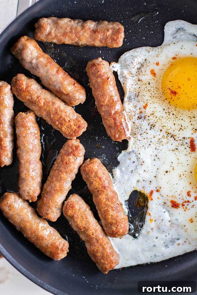 A frying pan with sausages and eggs cooking.