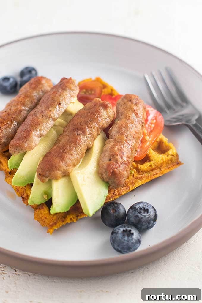 A sweet potato waffle with sliced avocado, sausage, and cherry tomatoes.