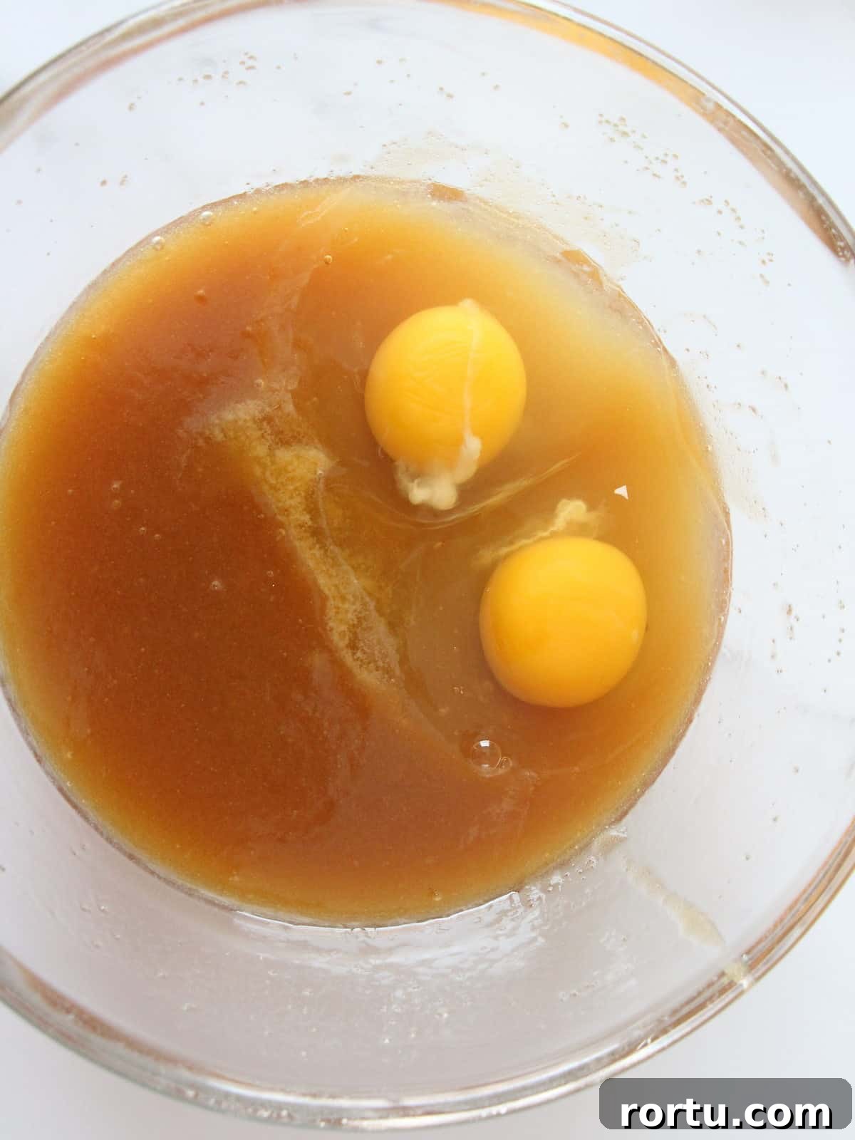 two whole cracked eggs inside melted butter with brown sugar getting ready to be mixed