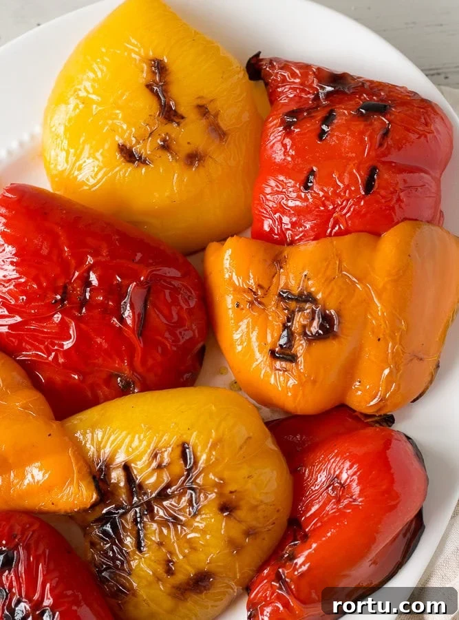 Red, yellow, and orange grilled bell pepper halves on a white platter.