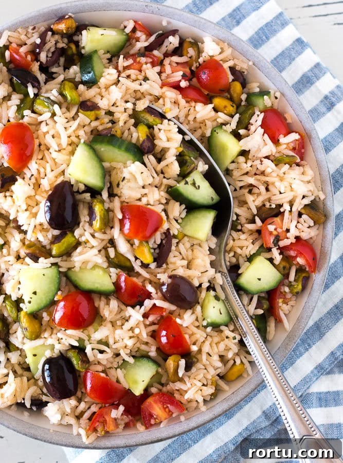 Top down shot of a gray bowl with Greek rice salad with a spoon in it.
