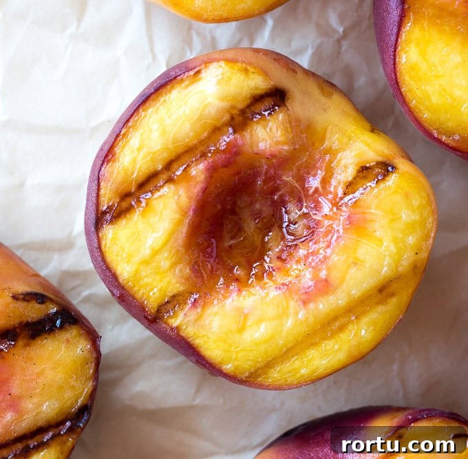 Top down close up of halved grilled peaches on white parchment paper.