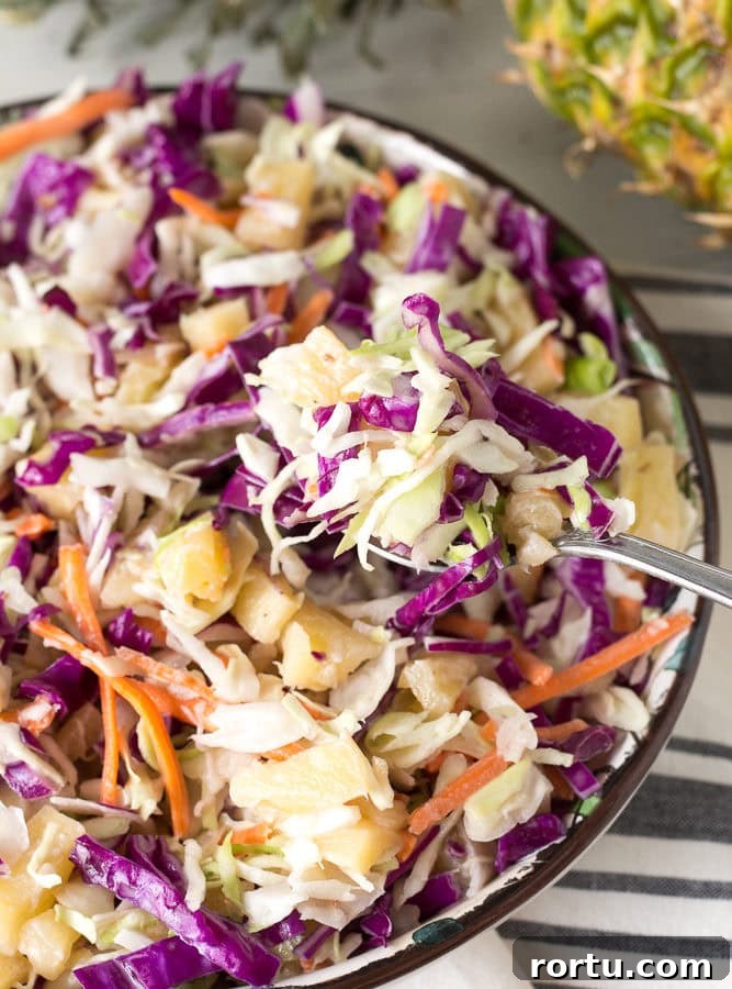 Close up of pineapple coleslaw in a bowl with a spoonful coming out.