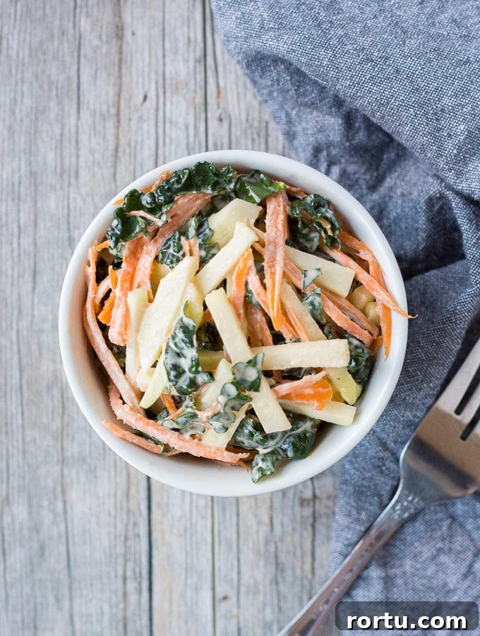 top down shot of kohlrabi, kale, and carrot coleslaw in a white bowl with a fork and gray towel