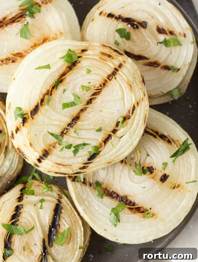 Close up of grilled onions on a gray plate with chopped fresh herbs sprinkled on top.