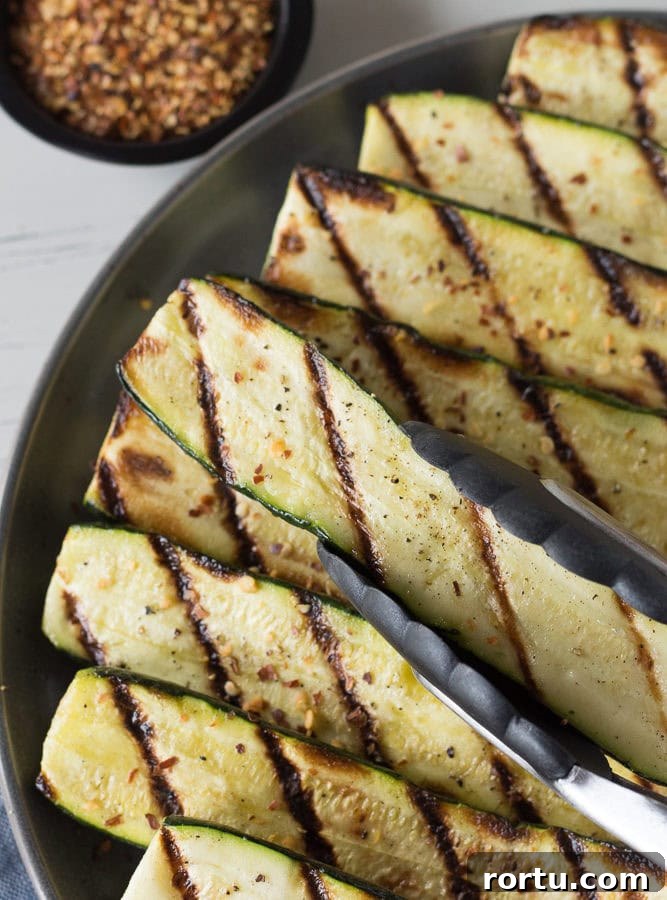Top down shot of a pair of tongs placing grilled zucchini on a gray plate.