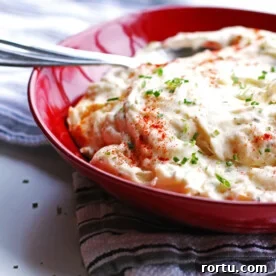 25 Perfect Side Dishes to Serve with Turkey Breast 3 Baked mashed potatoes in a red bowl with a spoon. The potatoes are garnished with chives.