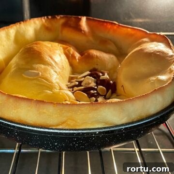 Puffed vanilla Dutch baby pancake topped with Nutella and flaked almonds in the oven.