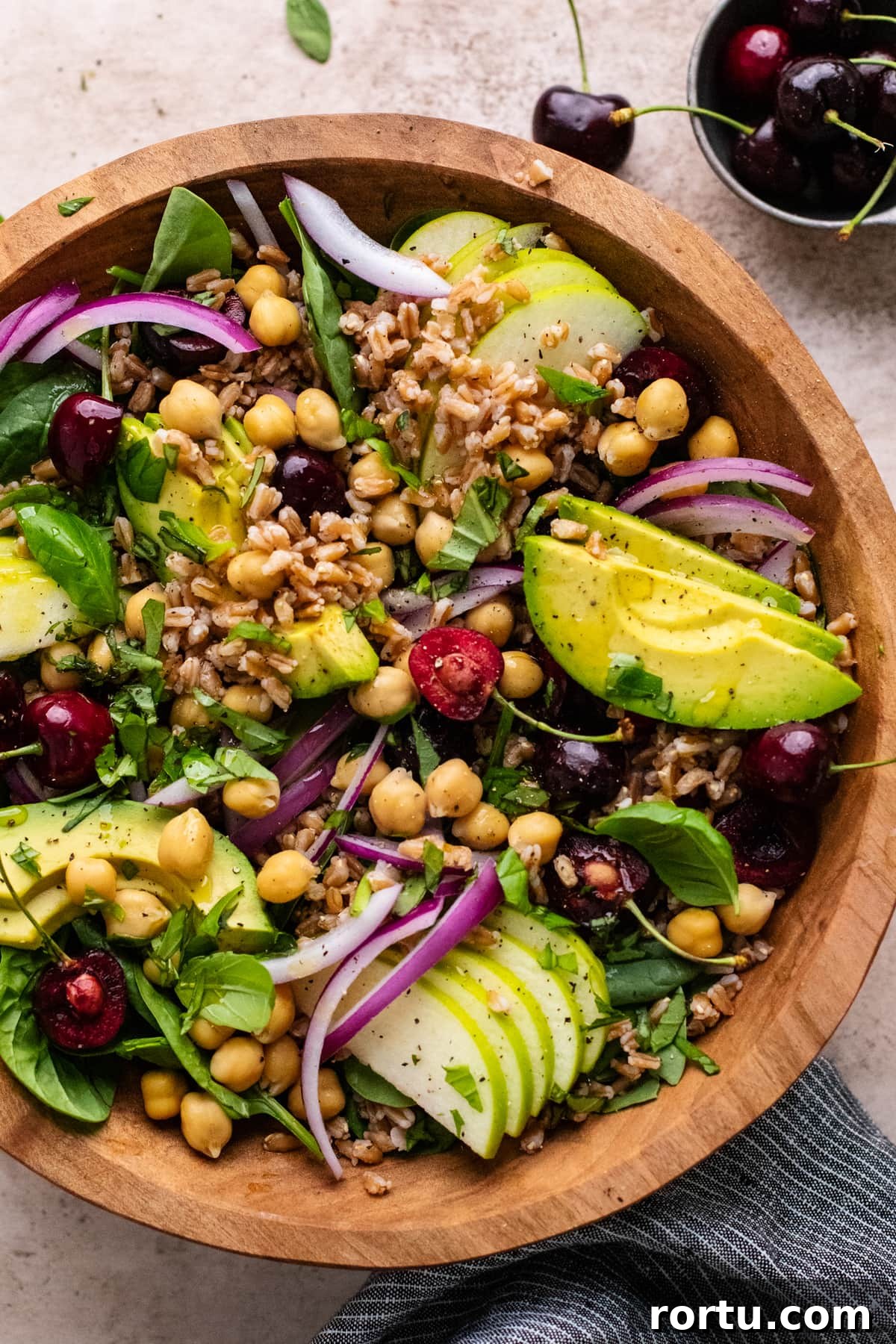 Summer Farro Salad with Cherries and Chickpeas for Picnic Menus 2 Farro salad with sliced avocado and cherries in a brown wooden bowl.