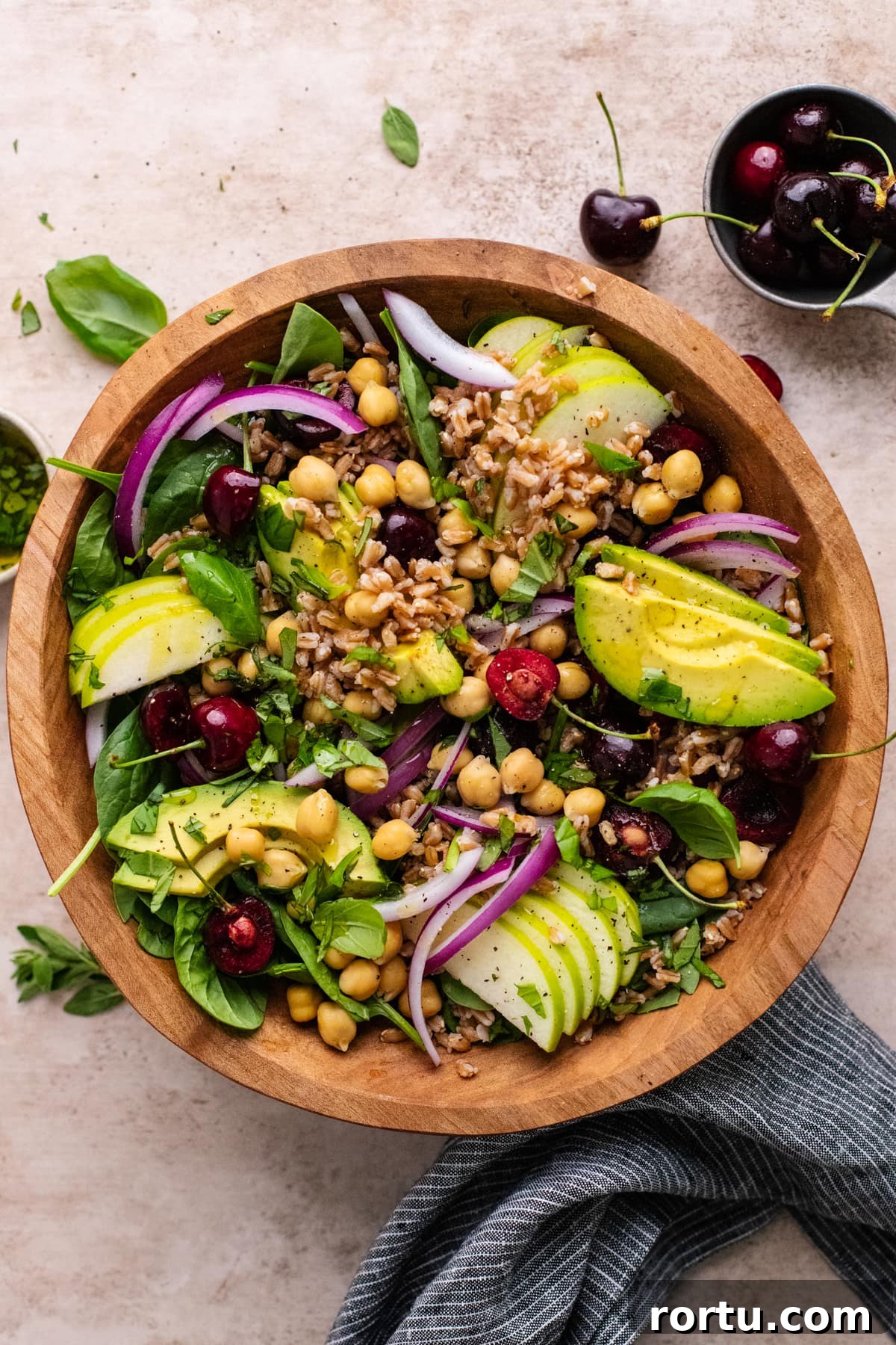Summer Farro Salad with Cherries and Chickpeas for Picnic Menus 8 wooden bowl filled with farro salad topped with sliced avocados and cherries.