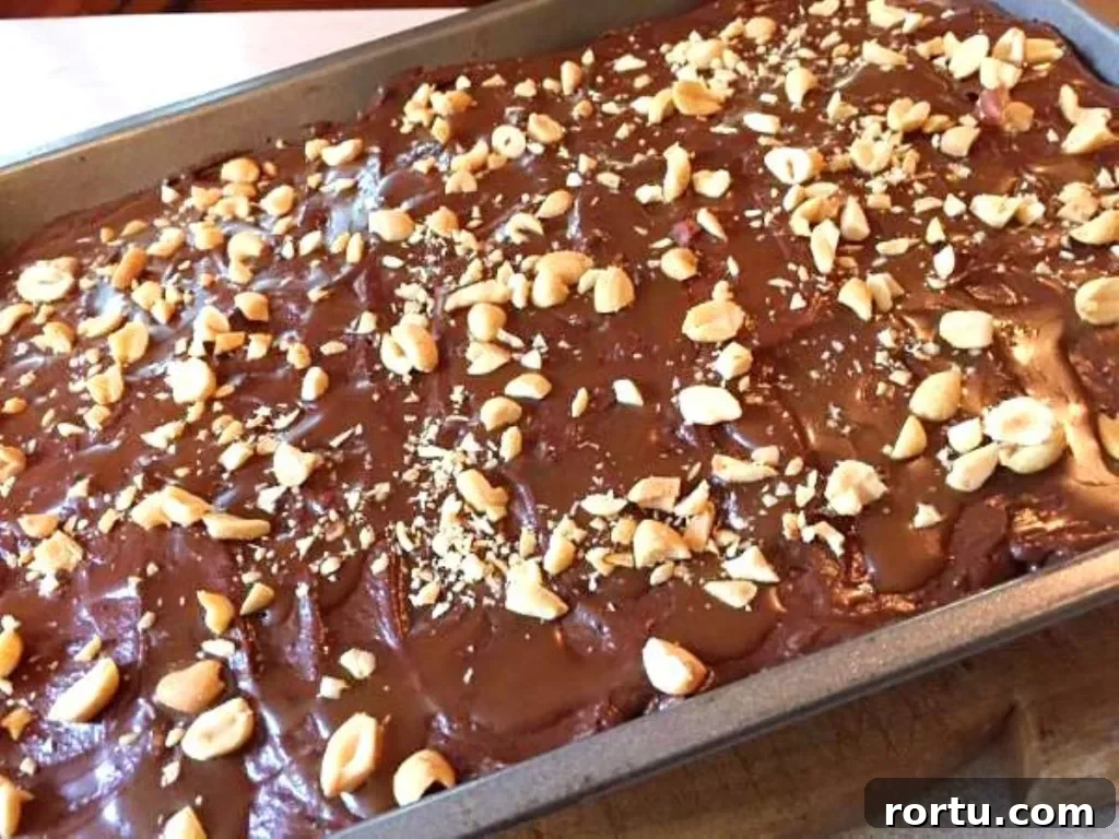 Chocolate caramel poke cake topped with thick chocolate frosting and chopped peanuts