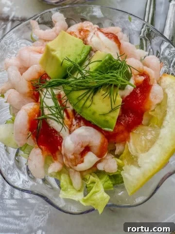 A small bowl of shrimp cocktail with lettuce, lemon, celery and avocado.