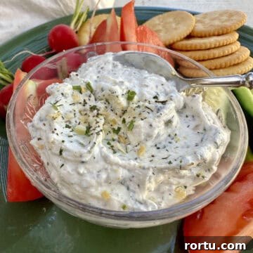 Garlic and herb dip in a dish on a plate with chopped vegetables and crackers.