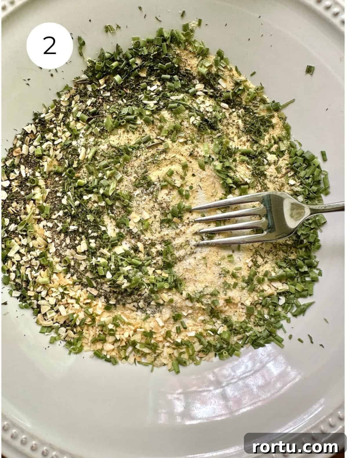 A fork blending dried herbs and salt on a plate.