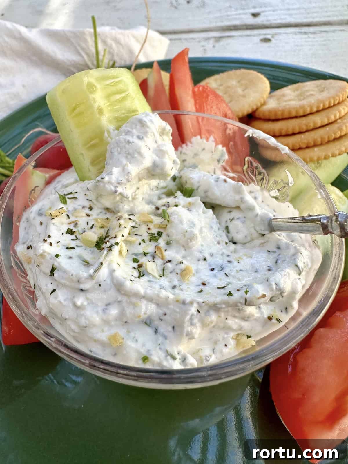 A slice of cucumber in a small bowl of herb and garlic dip on a plate.