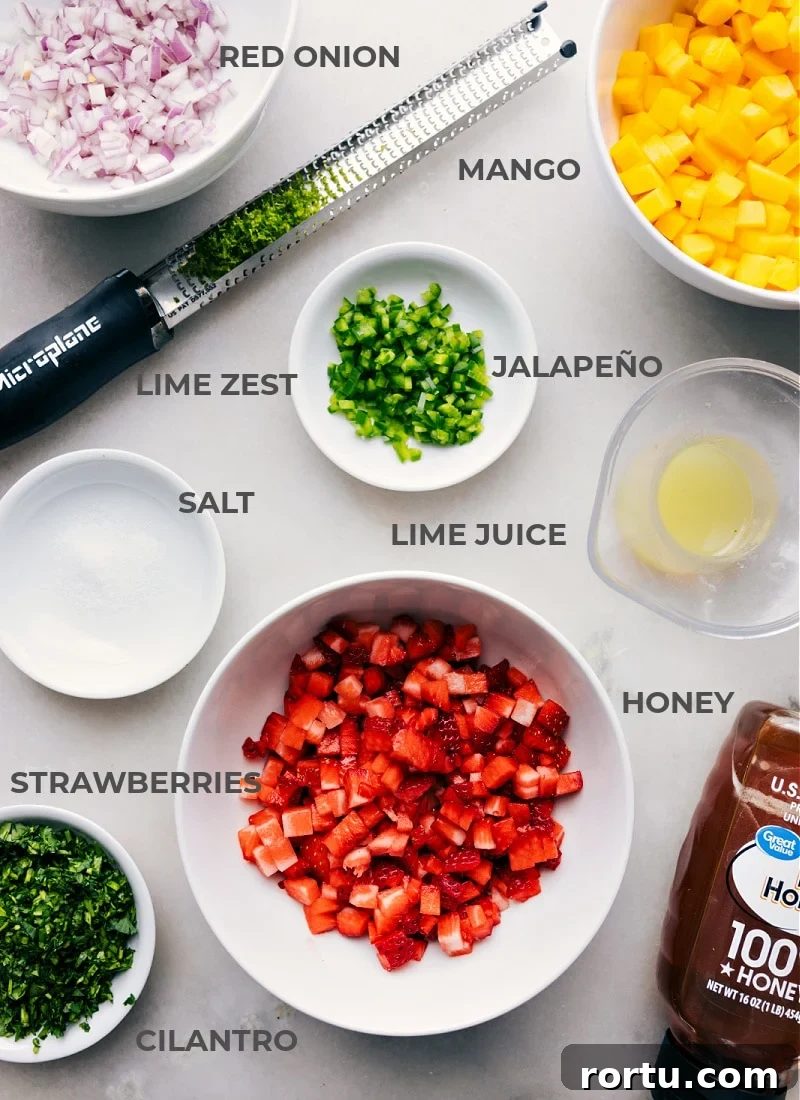 All the ingredients for strawberry mango salsa prepped and ready to go, including chopped onion, diced mango, minced jalapeño, lime juice, sliced strawberries, honey, salt, and lime zest.