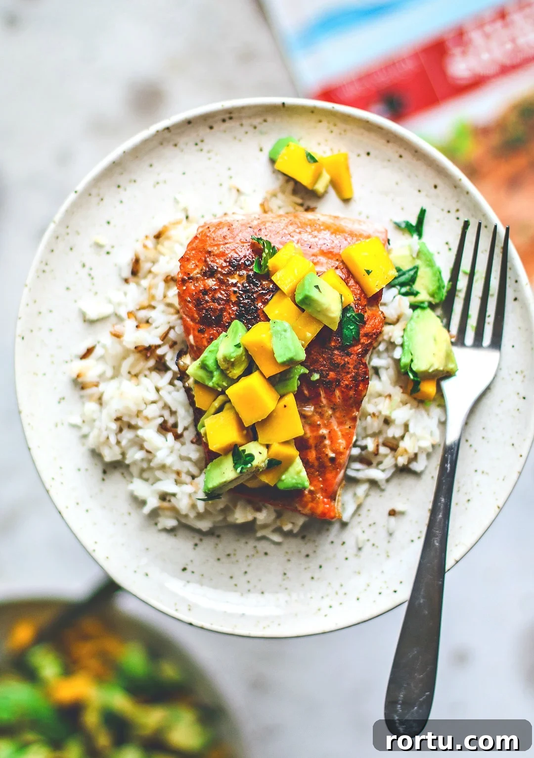 Close up of pan-seared salmon on plate over rice and topped with mango and avocado salsa.