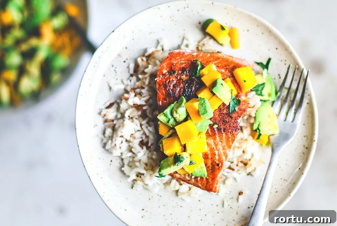 Pan-Seared Salmon on plate over rice and topped with mango and avocado salsa.