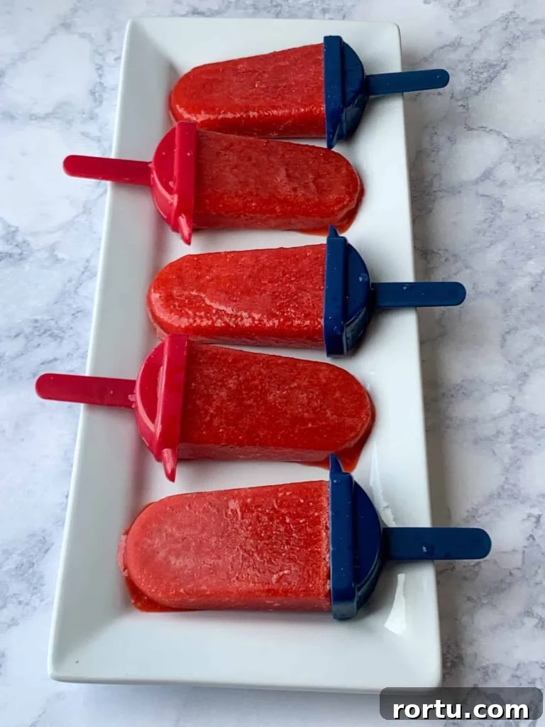 Five homemade strawberry popsicles on a white tray