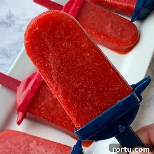 Strawberry popsicle on a blue stick with others on a white tray