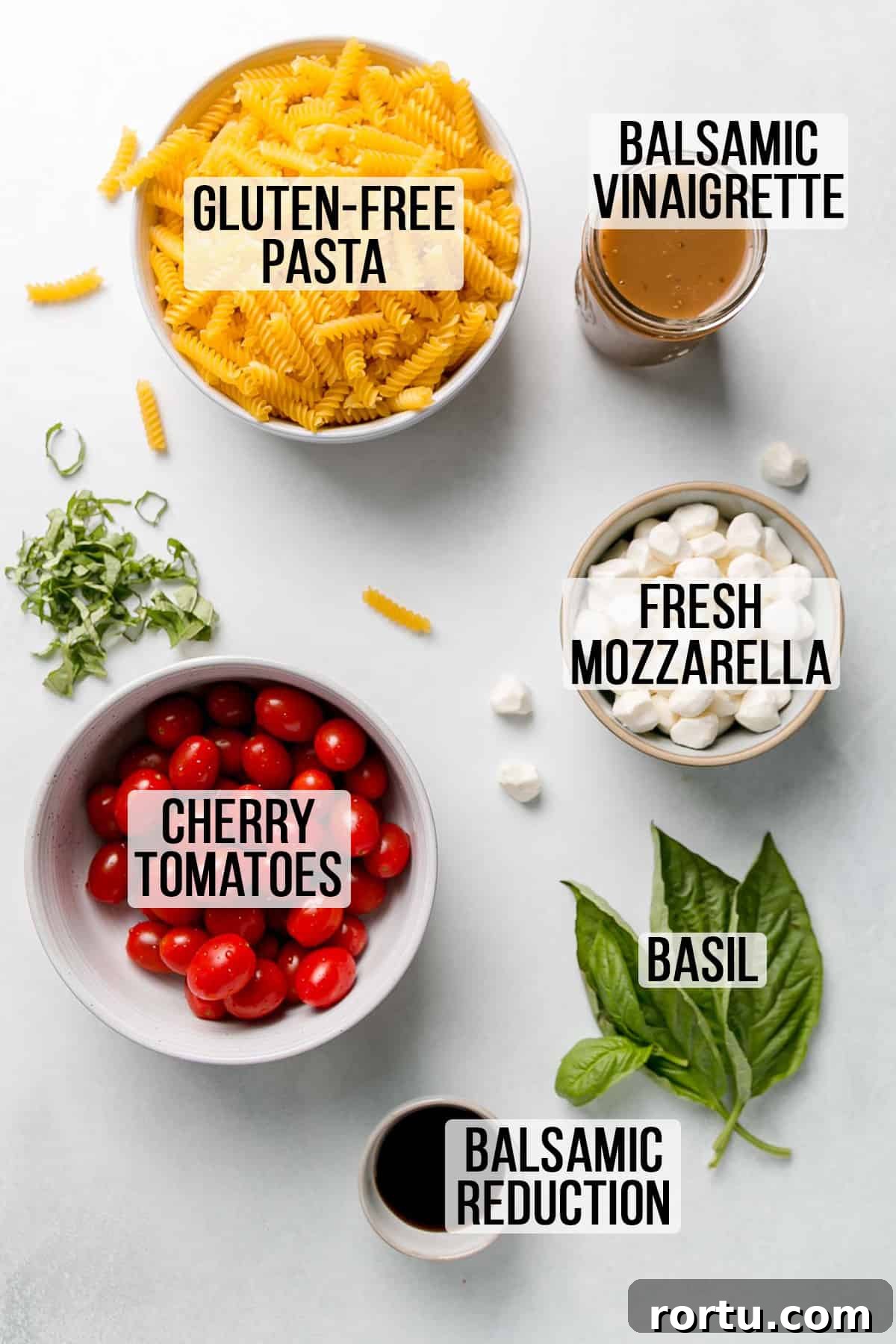Ingredients for caprese pasta salad measured out in bowls and laid on white surface.