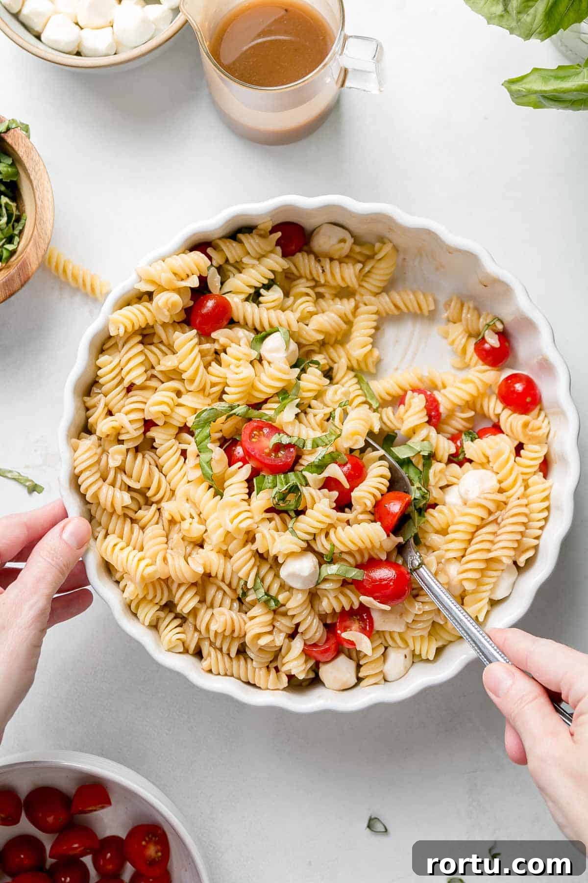 Stirring pasta salad ingredients together in serving dish.