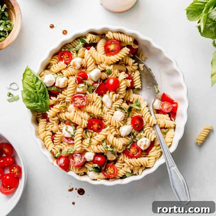 Gluten free caprese pasta salad with cherry tomatoes and basil in white dish.
