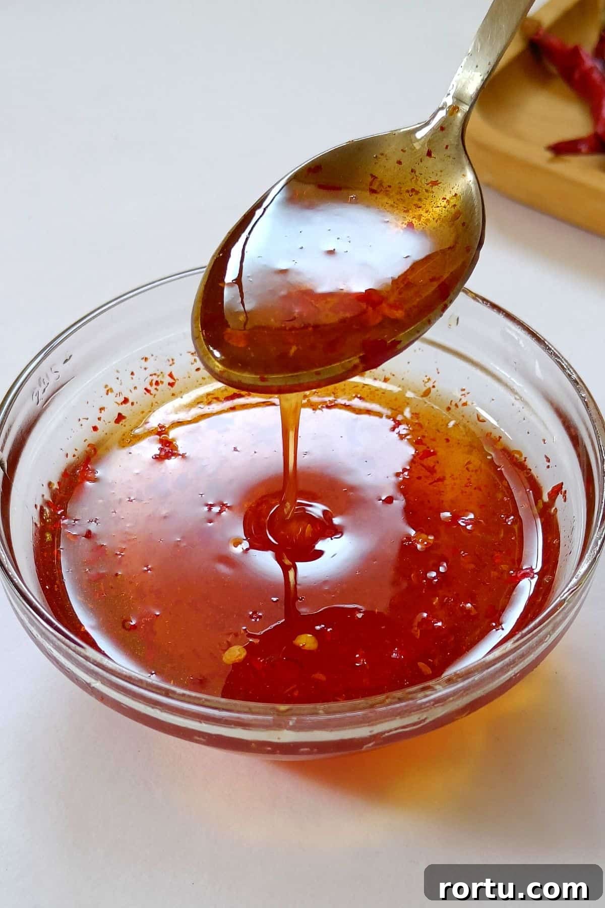 How to Make Homemade Hot Honey Sauce for Wings and Drizzle 5 Image showing spicy honey sauce dropping from a spoon to a bowl.