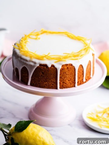 zesty lemon cake with icing and lemon peel decoration on a pink cake stand.