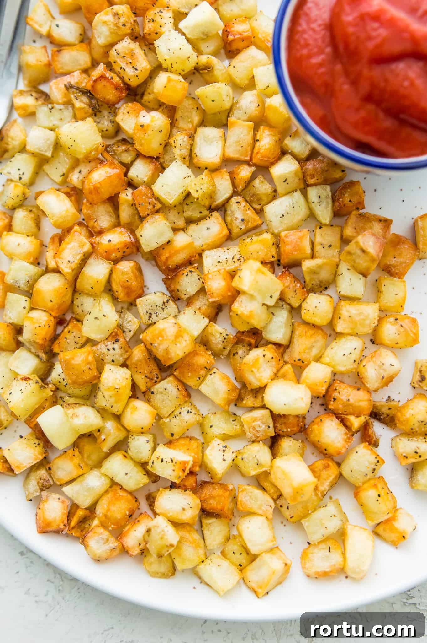 A plate of hash browns seasoned with black pepper with a side dish with ketchup in it.