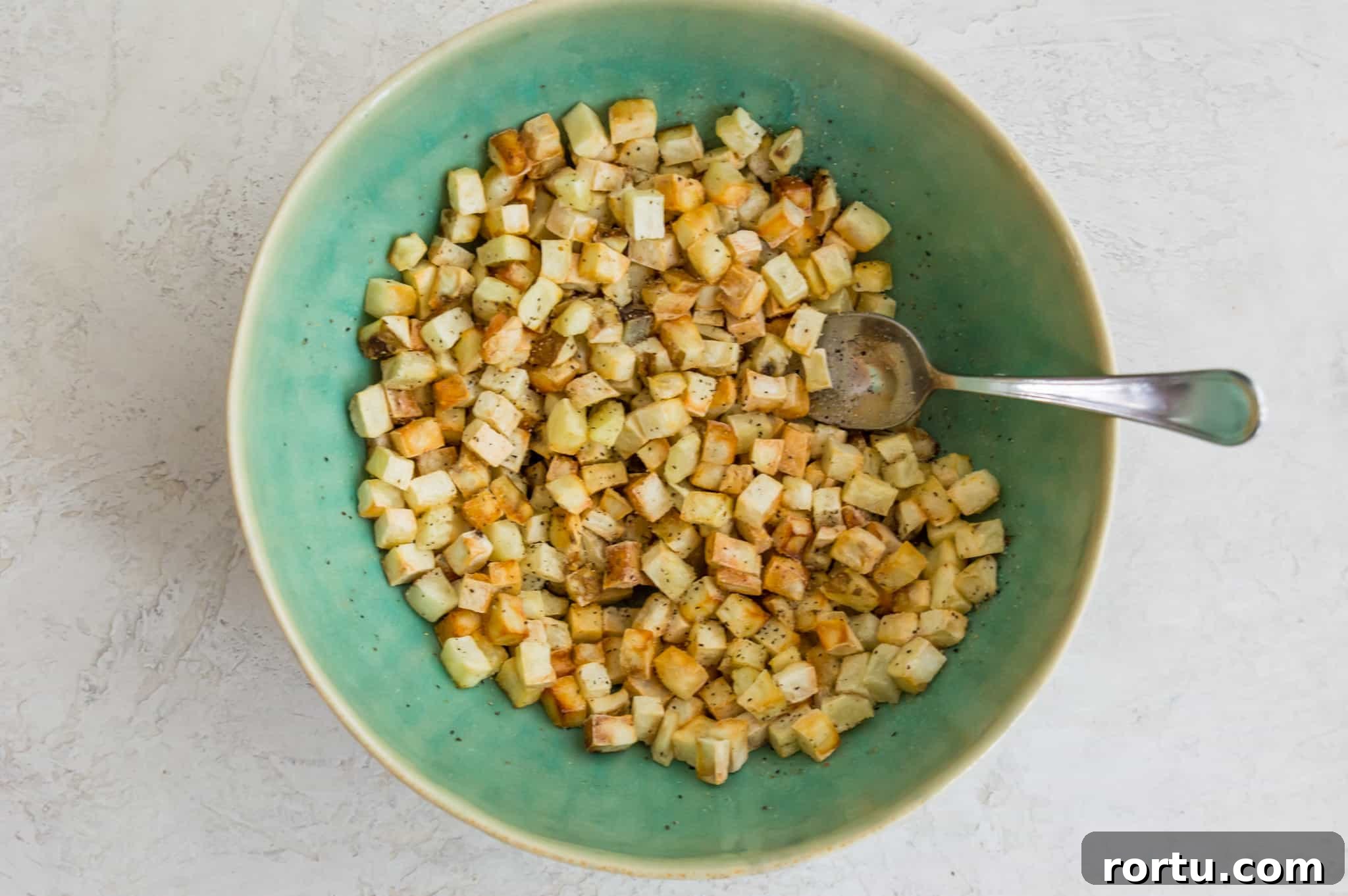 Cooked hash browns in a bowl with a spoon in it.