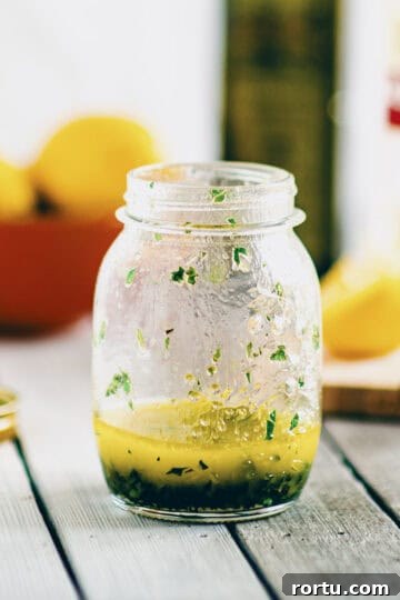 Greek salad dressing made with olive oil, lemon juice and herbs in a small glass jar.