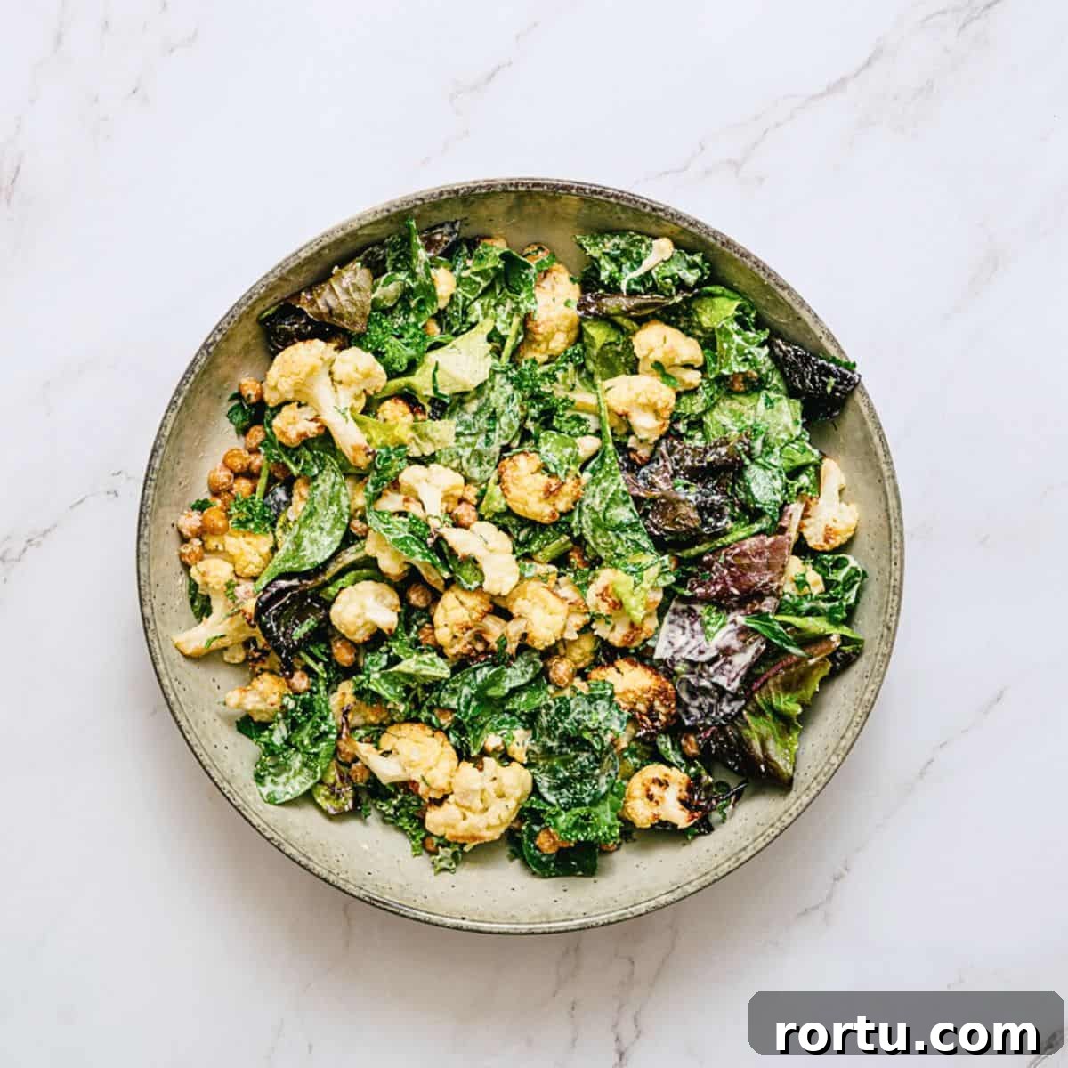 a bowl of roasted cauliflower salad on a white marble table.