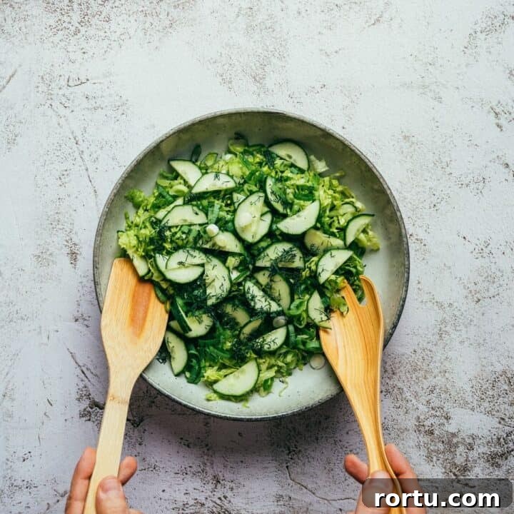 tossing a Greek green salad with wooden utensils in a large bowl.