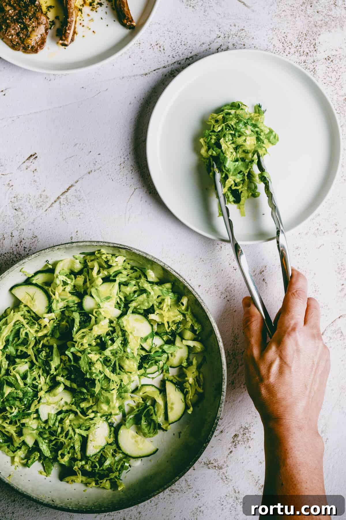 lettuce salad being served on a white plate with tongs.