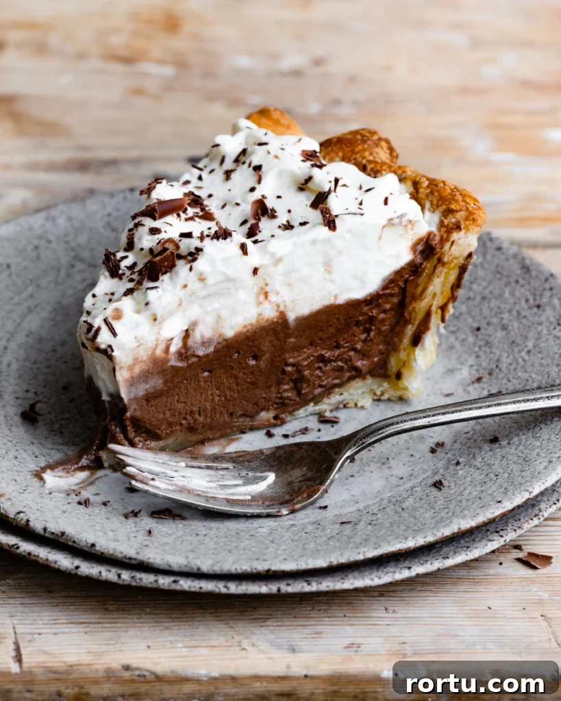 Slice of chocolate pie topped with whipped cream on a stack of plates next to a fork.