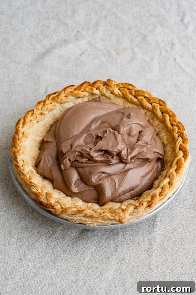 Chocolate mousse pie filling inside a baked pie crust on a table cloth.