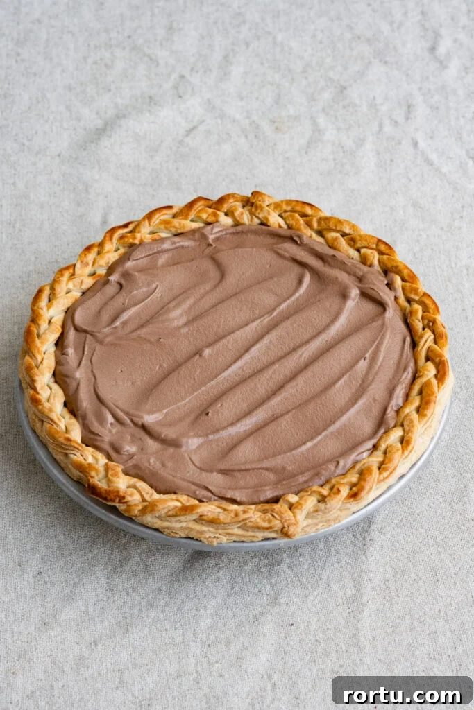 Chocolate french silk pie filling inside a baked pie crust on a tablecloth.